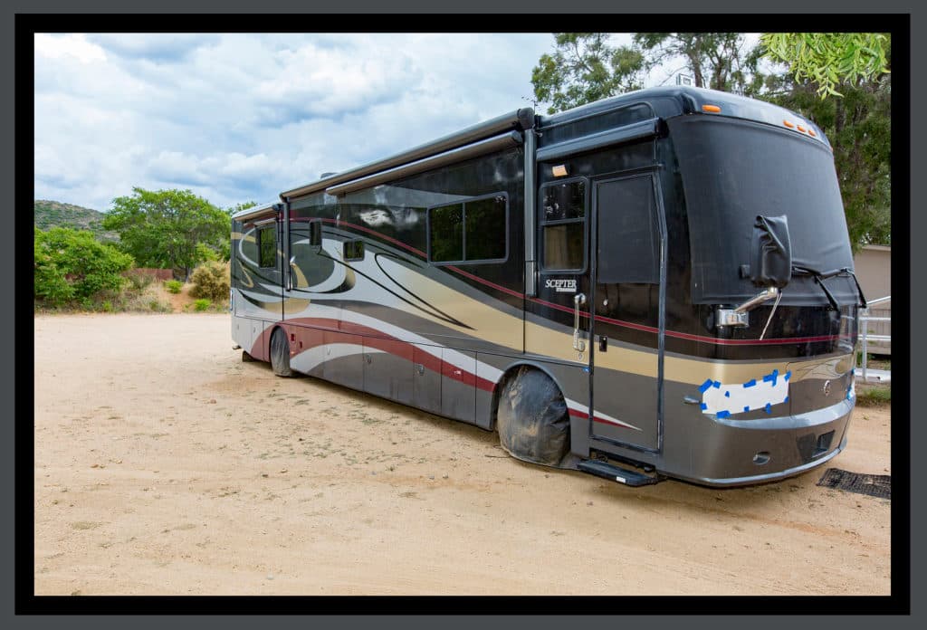Large motorhome parked on sandy ground with trees and hills in the background